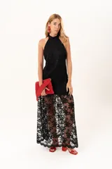 Vestido largo de encaje negro con cuello halter, compuesto por un minivestido base y una sobrefalda transparente de encaje con diseño floral.