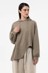 Buzo de punto oversize en color beige, con capucha, cordones largos ajustables y mangas largas amplias con puños elásticos. Presenta diseño asimétrico, más largo en la parte posterior.
