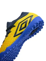 Championes de fútbol 5 Umbro modelo Ignis TF, con diseño de corte medio en tejido elástico color azul marino y cuerpo texturizado en color amarillo. Presenta suela de goma con tapones pequeños para césped sintético y logo de la marca en el lateral.