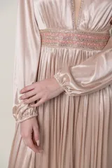 Vestido largo de satén color champagne, con escote en V profundo y mangas largas abullonadas con puños elásticos. Presenta apliques bordados con lentejuelas en el escote y la cintura.