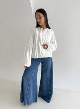 Blusa blanca con cuello mao y cierre frontal de botones de nácar. Presenta mangas largas abullonadas con puños elásticos y detalle de tablas verticales en el frente.