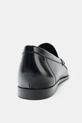 Mocasín plano de cuero negro con detalle de antifaz, copete subido y acabado fruncido en la parte delantera.