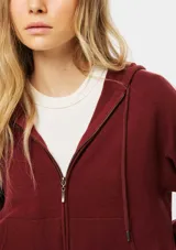 Campera de punto con cierre frontal, capucha con cordones ajustables y bolsillos tipo canguro. Presenta un diseño de manga larga con detalles acanalados en los laterales y puños.