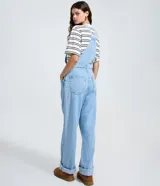 Peto de jean azul claro con corte recto, escote cuadrado, tirantes ajustables con hebillas metálicas y cierre lateral con botones. Cuenta con bolsillo frontal tipo parche y bolsillos laterales funcionales.