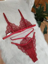 Conjunto de lencería de encaje rojo, compuesto por un bralette triangular con tirantes finos y una tanga con diseño de tiras cruzadas y detalles artesanales.