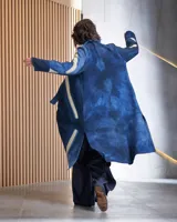 Tapado largo de lana merino afieltrada, color fucsia con diseño tie-dye artesanal en tonos claros y crudos. Tiene cuello que se prolonga a modo de cinto, aberturas laterales y bolsillos.