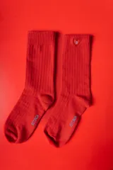 Medias de punto acanalado en color rojo intenso, con puño elástico. Presentan un detalle de corazón bordado con la letra R en la parte superior y el logo de la marca en la planta del pie.