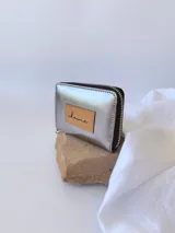 Billetera plateada de cuero con cierre metálico y monedero interno. Tiene un parche de cuero con la inscripción 'Chowie'.