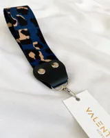 Llavero de tela con estampado animal print en tonos azul, negro y beige. Incluye tira de cuero sintético negro y gancho metálico plateado.