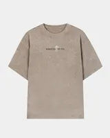 Remera oversize de color marrón topo con efecto acid wash, cuello redondo y manga corta. Cuenta con un pequeño estampado gráfico frontal con el texto 'WAKE UP IND' y una calavera.