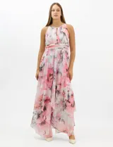 Vestido largo de fiesta con estampado floral en tonos rosa y gris sobre fondo blanco. Presenta cuello halter con abertura tipo lágrima, cintura drapeada y falda amplia con capas asimétricas y bajo en picos. Confeccionado en tejido ligero con forro interior.