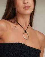 Collar con dije colgante de forma orgánica e irregular, acabado dorado, suspendido de un cordón negro de algodón natural.