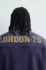 Remera de manga corta con corte relajado, confeccionada en tejido de algodón con textura tipo waffle. Presenta un efecto de lavado desgastado en color azul oscuro y estampado gráfico a contraste en el frente.