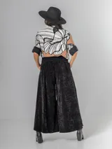 Pantalón tipo palazzo de corte oversized, confeccionado en tela con textura aterciopelada en color negro. Presenta cintura alta con pinzas, bolsillos laterales y un cinturón ancho integrado con hebilla al tono.