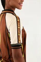 Camiseta deportiva estilo polo de color marrón con diseño estampado, cuello negro y detalles en blanco y verde flúor. Cuenta con mangas cortas y escudo frontal con las iniciales 'ETC' flanqueadas por aves.