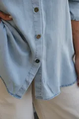 Camisa de jean en tono celeste claro, de corte holgado y diseño oversize. Presenta cuello clásico, cierre frontal con botones y mangas largas con puños con detalle de volado sutil.