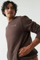 Buzo de felpa color gris claro, con cuello redondo, mangas largas y costuras a contratono. Presenta lettering estampado en el pecho, bolsillos laterales y logo en grifa de goma.