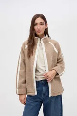 Campera de sherpa color marrón con diseño capitoneado, cierre frontal completo y detalles en color blanco. Presenta cuello alto, bolsillos laterales y puños elásticos.