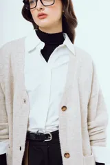 Cardigan de punto color beige, con escote en V, cierre frontal de botones carey, mangas largas y bolsillos frontales aplicados.