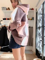 Campera tipo hoodie confeccionada en tejido de corderito sintético con diseño de bloques geométricos en tonos marrón, rosado y blanco. Presenta capucha amplia, corte oversize y mangas largas.
