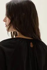 Blusa de algodón de corte holgado, con cuello redondo fruncido y cierre de lazo frontal. Presenta mangas largas con puños elásticos.