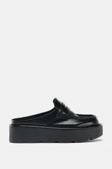 Mocasín destalonado de estilo mule, color negro, con diseño de antifaz y suela de plataforma dentada tipo chunky.