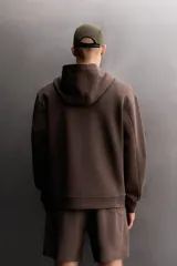 Sudadera de hombre Zara Athleticz de ajuste relajado (relaxed fit), color marrón, confeccionada en tejido técnico compacto con mezcla de algodón y elasticidad. Cuenta con cuello con capucha ajustable con cordones negros, manga larga, bolsillo frontal tipo canguro con un pequeño bolsillo termofijado con cierre, y acabados con rib en puños y cintura.