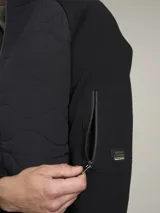 Campera azul marino con cierre frontal, cuello alto y bolsillos laterales con cierre. Tiene un parche rojo con cierre en la manga izquierda y un diseño acolchado en la parte delantera.