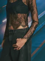 Top de encaje negro con diseño floral, manga larga y cuello redondo. Presenta un acabado festoneado en el ruedo y mangas.