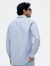 Camisa Oxford de manga larga en color celeste, con cuello clásico, cierre frontal de botones y bolsillo en el pecho.