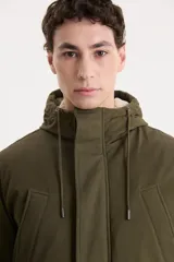 Campera parka larga color verde militar con capucha forrada en piel sintética. Tiene cierre frontal con cremallera y botones a presión, cuatro bolsillos delanteros con solapa y puños ajustables con botones.