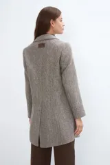 Saco corto entallado de lana fina, con cuello solapa, manga larga y cierre frontal con botones. Presenta un diseño clásico con textura de espiga en tonos tierra.