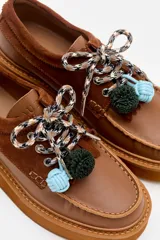 Zapato tipo mocasín de plataforma color bordó, confeccionado en una combinación de cuero liso y gamuza. Presenta cordones bicolores con detalle de borlas decorativas en el empeine.