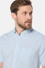 Camisa de lino de manga corta con estampado a cuadros en tonos celestes y blancos, cuello con botones y bolsillo ojal en el pecho.