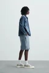 Bermuda de denim de algodón, color verde claro lavado, de corte recto y tiro medio. Presenta cinco bolsillos y cierre frontal con cremallera y botón.