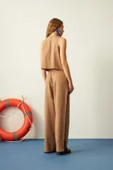 Pantalón marrón de corte recto, con cintura elastizada y cordón ajustable. Presenta mostacillas decorativas en los laterales.