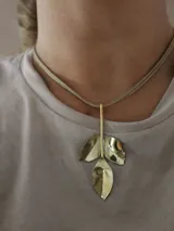 Collar con cadena doble color beige y dije colgante dorado con forma de tres hojas.