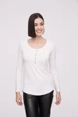 Remera blanca de manga larga, entallada, con cuello redondo y una hilera de botones en el frente. Incluye un pequeño bolsillo decorativo en el pecho.