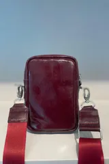 Bolso tipo bandolera de cuero vacuno color suela, con cierre frontal y compartimento principal. Incluye correa de cinta regulable y herrajes metálicos plateados.