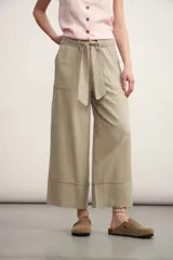 Pantalón de corte ancho y tiro alto, color beige, con cintura elástica y lazo ajustable del mismo tejido. Presenta bolsillos laterales y dobladillo ancho en la parte inferior.