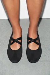Bailarina de estilo deportivo en color negro, confeccionada en una combinación de materiales textiles y sintéticos. Presenta tiras elásticas cruzadas en el empeine, punta redonda y suela de goma plana.