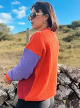 Sweater de punto con diseño color block, presentando un frente en tono verde oscuro melange con un bordado floral en el hombro, y mangas en color fucsia vibrante. Posee cuello redondo y puños acanalados.