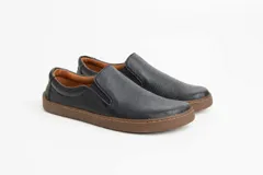 Zapatillas tipo slip-on de gamuza color beige, con diseño barefoot y suela de corcho texturizado. Presenta elásticos laterales negros para un calce fácil.