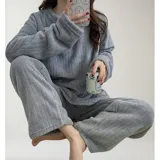 Conjunto de pijama de dos piezas confeccionado en tela de plush texturizada con diseño de rayas verticales en relieve. Incluye una remera de manga larga con cuello redondo y un pantalón de corte holgado. La remera presenta un pequeño bordado decorativo en el pecho.