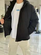 Campera puffer impermeable color beige con capucha desmontable con cordones negros, cierre frontal con cremallera y solapa con botones a presión.