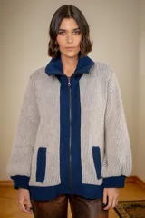Campera de punto tipo cárdigan con cierre frontal de doble cursor, confeccionada en lana. Presenta un diseño bicolor con cuerpo en tono gris claro y detalles en azul marino en el cuello, la franja central, los bolsillos y los puños. Posee mangas largas con terminación ajustada y bolsillos frontales.