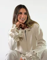 Saco de punto color beige con cierre frontal, mangas largas y puños voluminosos con detalles de volados tejidos.