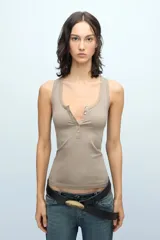 Musculosa fitted color tostado, confeccionada en pima de algodón peruano con lycra. Presenta escote en U, espalda deportiva y cartera de botones a tono personalizados. Incluye bordado marcario a tono en el frente.