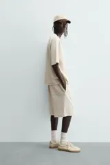 Bermuda de corte relajado, color crema o blanco roto, con textura acanalada (canalé). Presenta cintura elástica ajustable con cordón, bolsillos de vivo frontales y un bolsillo plastrón trasero.