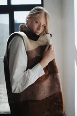 Chaleco largo de piel de oveja con bloques de color en tonos marrón, beige y blanco. Tiene cuello solapa y cierre con un botón forrado en piel.